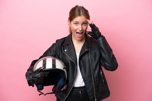 Young caucasian woman with a motorcycle helmet isolated on pink background with surprise expression