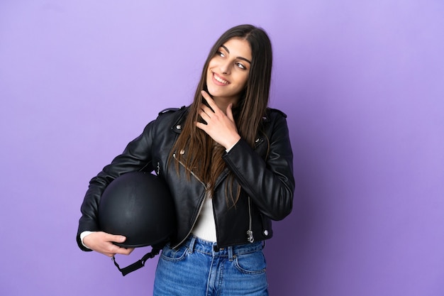 Young caucasian woman with a motorcycle helmet isolated on purple background looking up while smiling