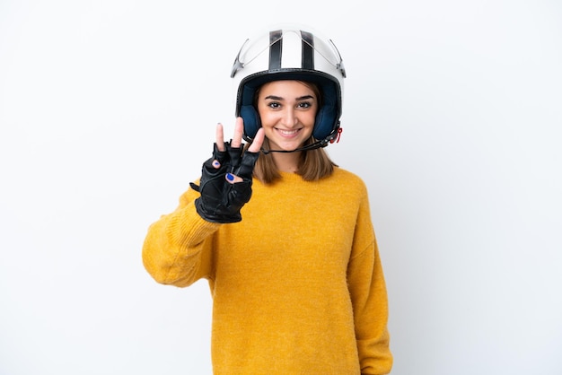 Молодая кавказская женщина в мотоциклетном шлеме на белом фоне счастлива и считает три пальцами