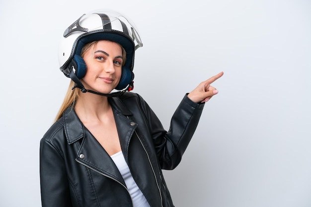 Young caucasian woman with a motorcycle helmet isolated on\
white background pointing finger to the side