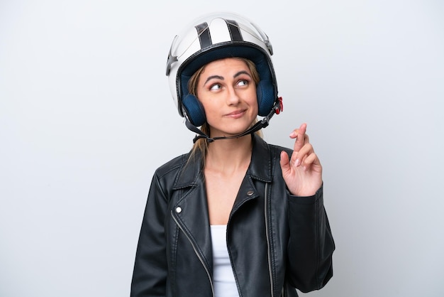 Young caucasian woman with a motorcycle helmet isolated on\
white background with fingers crossing and wishing the best