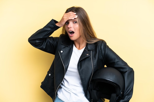 Young caucasian woman with a motorcycle helmet isolated on yellow background doing surprise gesture while looking to the side