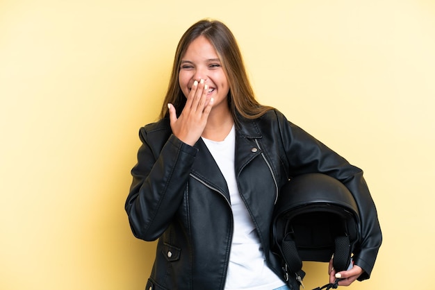 Young caucasian woman with a motorcycle helmet isolated on yellow background happy and smiling covering mouth with hand