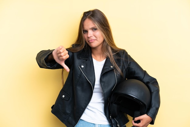 Foto giovane donna caucasica con un casco da motociclista isolato su sfondo giallo che mostra il pollice verso il basso con espressione negativa