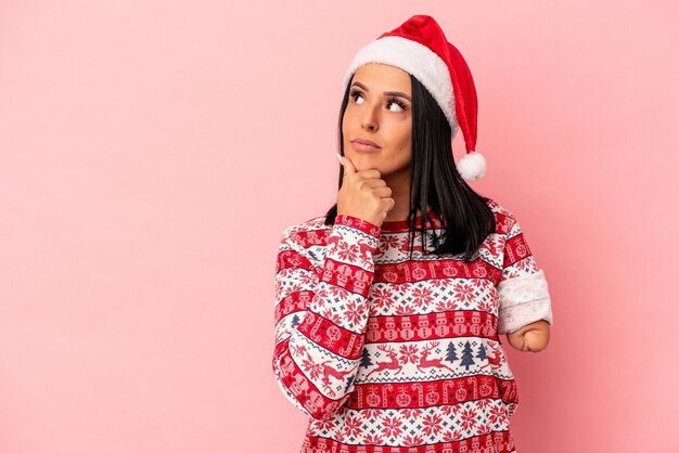 Young caucasian woman with one arm celebrating Christmas isolated on pink background looking sideways with doubtful and skeptical expression.