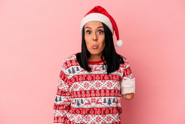 Young caucasian woman with one arm celebrating Christmas isolated on pink background shrugs shoulders and open eyes confused.