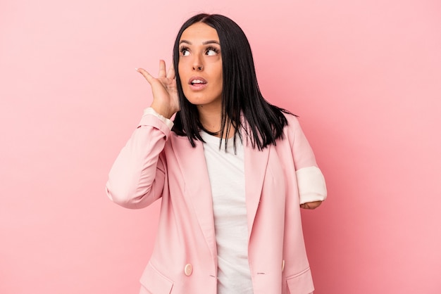 Young caucasian woman with one arm isolated on pink background trying to listening a gossip.