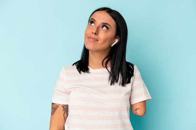 Young caucasian woman with one arm listening to music with wireless headphones isolated on blue background dreaming of achieving goals and purposes