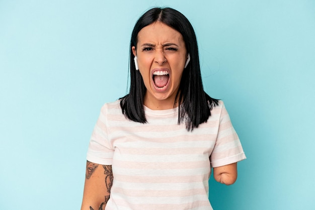 Young caucasian woman with one arm listening to music with wireless headphones isolated on blue background screaming very angry and aggressive.