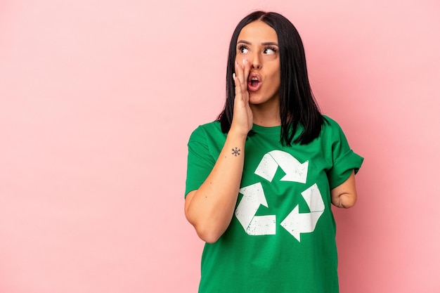 Young caucasian woman with one arm recycled waste isolated on pink background is saying a secret hot braking news and looking aside