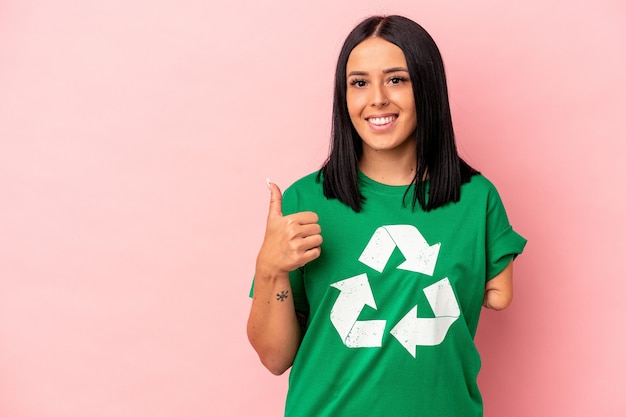 Young caucasian woman with one arm recycled waste isolated on pink background smiling and raising thumb up