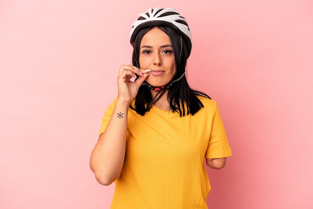 秘密を保持している唇に指でピンクの背景に分離された自転車のヘルメットを身に着けている片方の腕を持つ若い白人女性。
