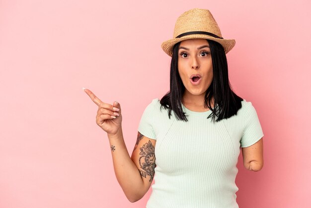 Young caucasian woman with one arm wearing a summer hat isolated on pink background pointing to the side