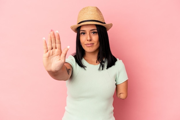 Young caucasian woman with one arm wearing a summer hat isolated on pink background standing with outstretched hand showing stop sign, preventing you.