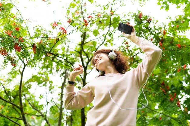 Foto giovane donna caucasica con un sorriso perfetto, labbra carnose, occhiali, auricolari, carta, passeggiate nella natura, ascoltare musica e balli