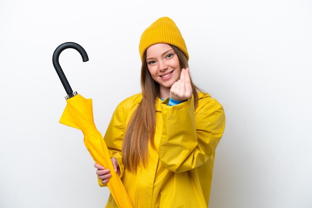 防雨コートとお金のジェスチャーを作る白い背景で隔離の傘を持つ若い白人女性