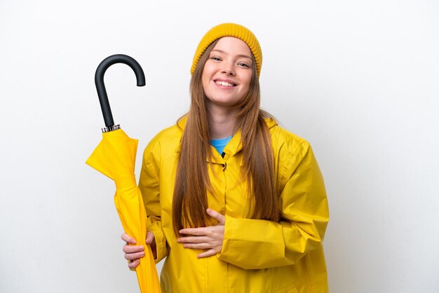 Young caucasian woman with rainproof coat and umbrella isolated on white background smiling a lot