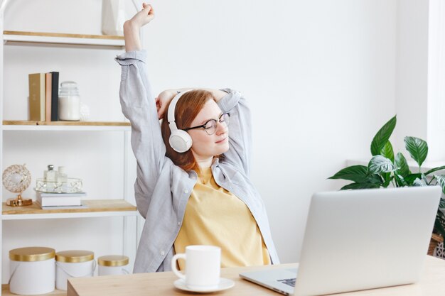 Young Caucasian woman with red hair resting at the computer listening to music