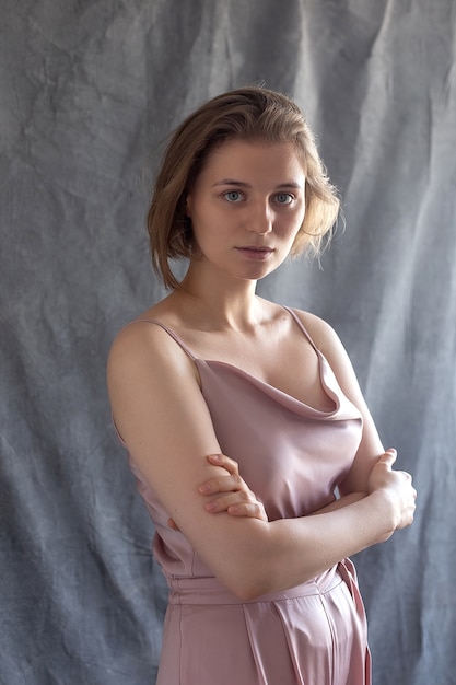 Photo young caucasian woman with short hair posing in pink suit, standing in front of fabric