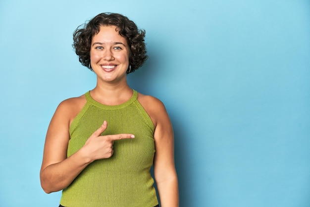 Young Caucasian woman with short hair smiling and pointing aside showing something at blank space