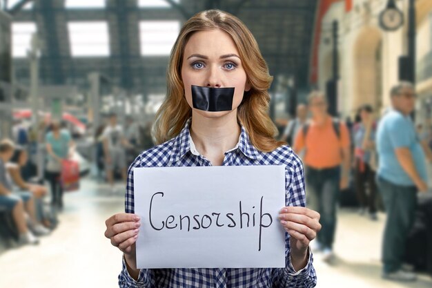 Young caucasian woman with taped mouth holding banner with inscription Censorship.