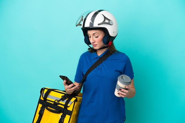 Photo young caucasian woman with thermal backpack isolated on white background holding coffee to take away and a mobile