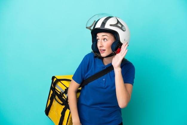 Young caucasian woman with thermal backpack isolated on white background listening to something by putting hand on the ear