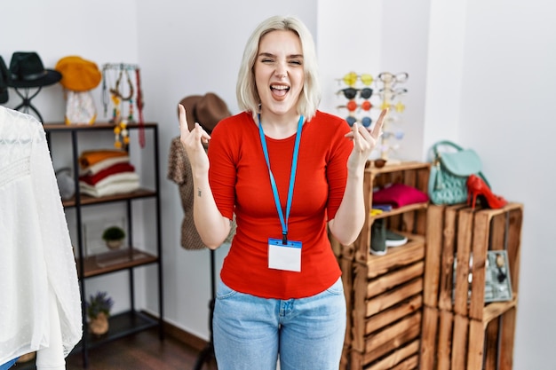 Young caucasian woman working as manager at retail boutique shouting with crazy expression doing rock symbol with hands up music star heavy concept