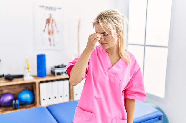 Young caucasian woman working at pain recovery clinic tired rubbing nose and eyes feeling fatigue and headache. stress and frustration concept.