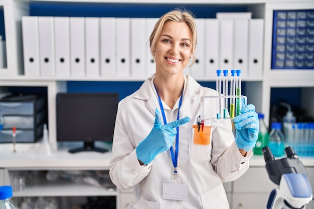 試験管を保持している科学者の実験室で働く若い白人女性の手と指で幸せな指差しを笑顔