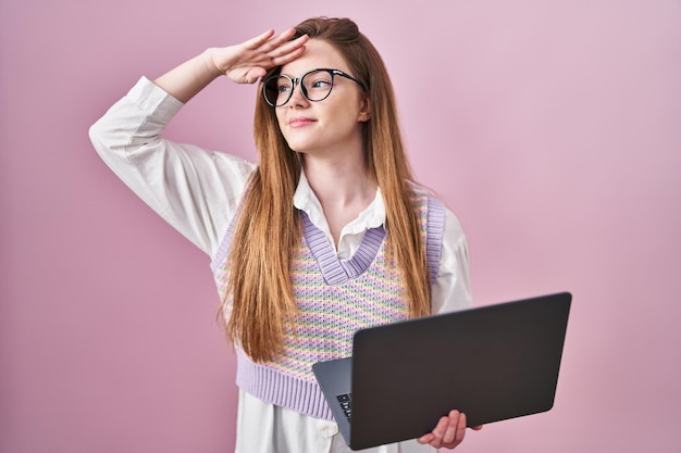 Young caucasian woman working using computer laptop very happy and smiling looking far away with hand over head. searching concept.