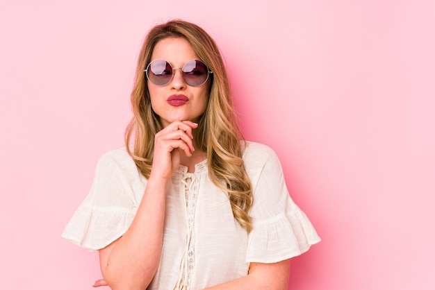 Young caucian woman with glasses isolated on pink thinking and looking up, being reflective, contemplating, having a fantasy.