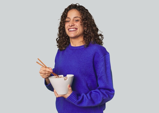 A young caucsian woman eating noddles with chopsticks very happy