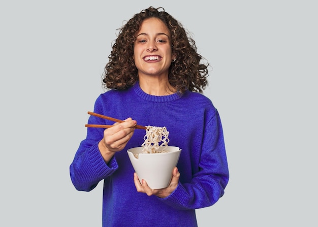 A young caucsian woman eating noddles with chopsticks very happy