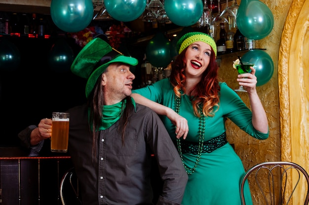 Молодые празднуют Патрик день веселье бар карнавал головные уборы девушка мужчина пиво коктейль зеленая одежда шляпа улыбка красивый гном