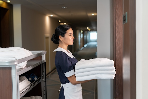 Young chambermaid bringing clean sheets to one of hotel clients