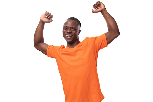 Young charismatic positive american guy with a short haircut dressed in an orange tshirt on a white