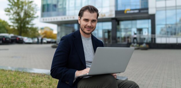 Young charismatic successful businessman working on laptop outside