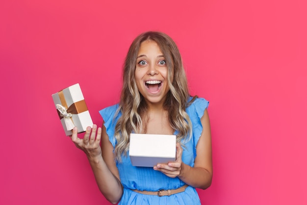 A young charmig amazed excited blonde woman is happy with the gift she received on a pink background