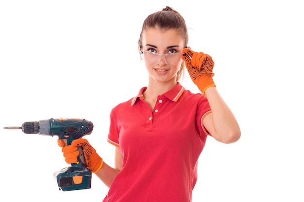 Young charming builder woman in uniform with drill in hands makes renovation isolated on white wall