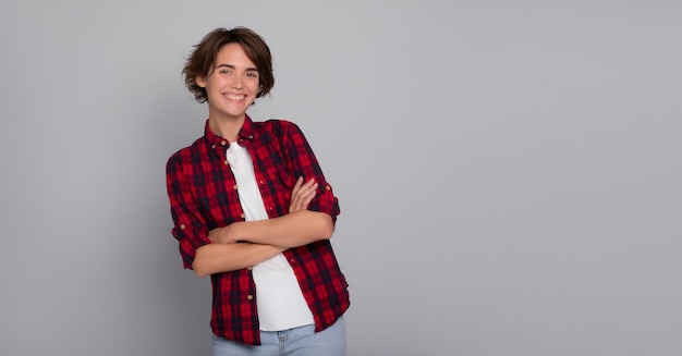 Young charming confident smiling woman student with arms crossed in checkered shirt isolated on gray background