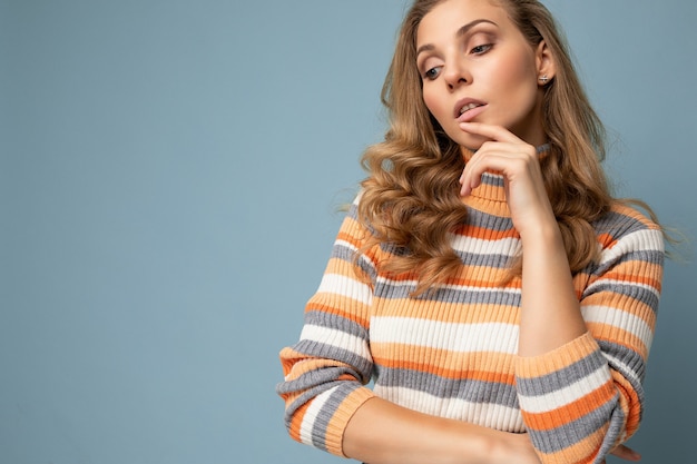 Young charming fascinating beautiful sexy positive blonde woman wearing casual striped pullover isolated over blue background with free space.