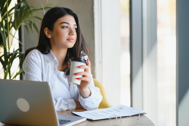 Young charming female freelancer using laptop computer for
distance job while sitting in modern coffee shop interior beautiful
caucasian woman working on netbook during morning breakfast in cafe
bar