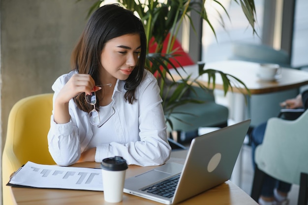 Young charming female freelancer using laptop computer for
distance job while sitting in modern coffee shop interior beautiful
caucasian woman working on netbook during morning breakfast in cafe
bar