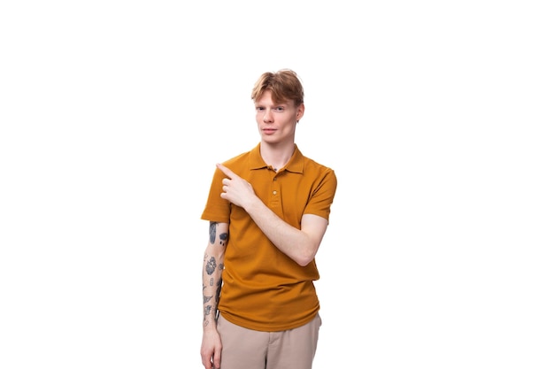 Young charming redhaired man dressed in a mustard tshirt points his hand to the side