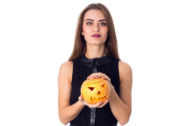 Young charming woman in black dress holding a pumpkin in her hands on white background in studio