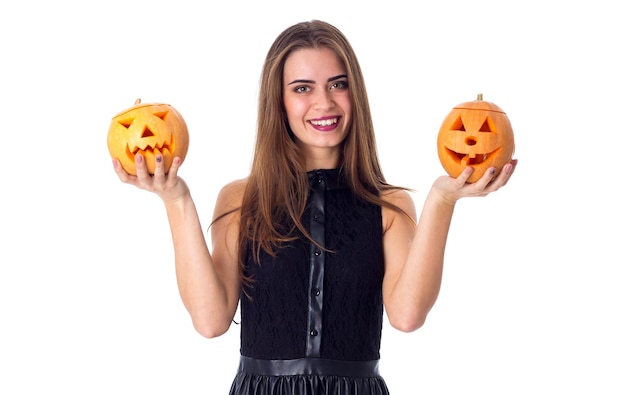 Young charming woman in black dress holding a pumpkin in her hands on white background in studio