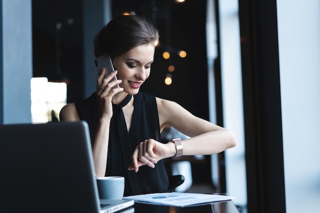 Giovane donna affascinante che chiama con il cellulare mentre è seduta al bar durante il tempo libero, una donna attraente che parla con il cellulare mentre riposa al bar.