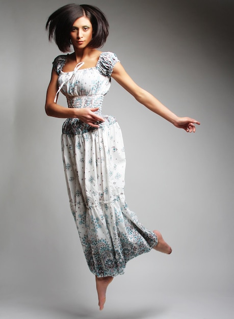 Young charming woman in chiffon dress jumping over grey backgro