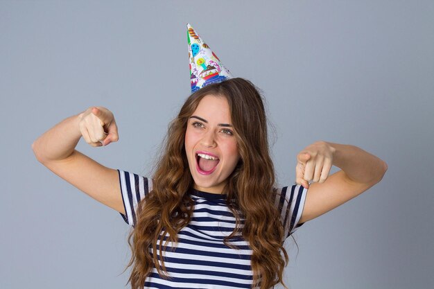 Young charming woman wearing in stripped Tshirt and celebration cap on grey background in studio